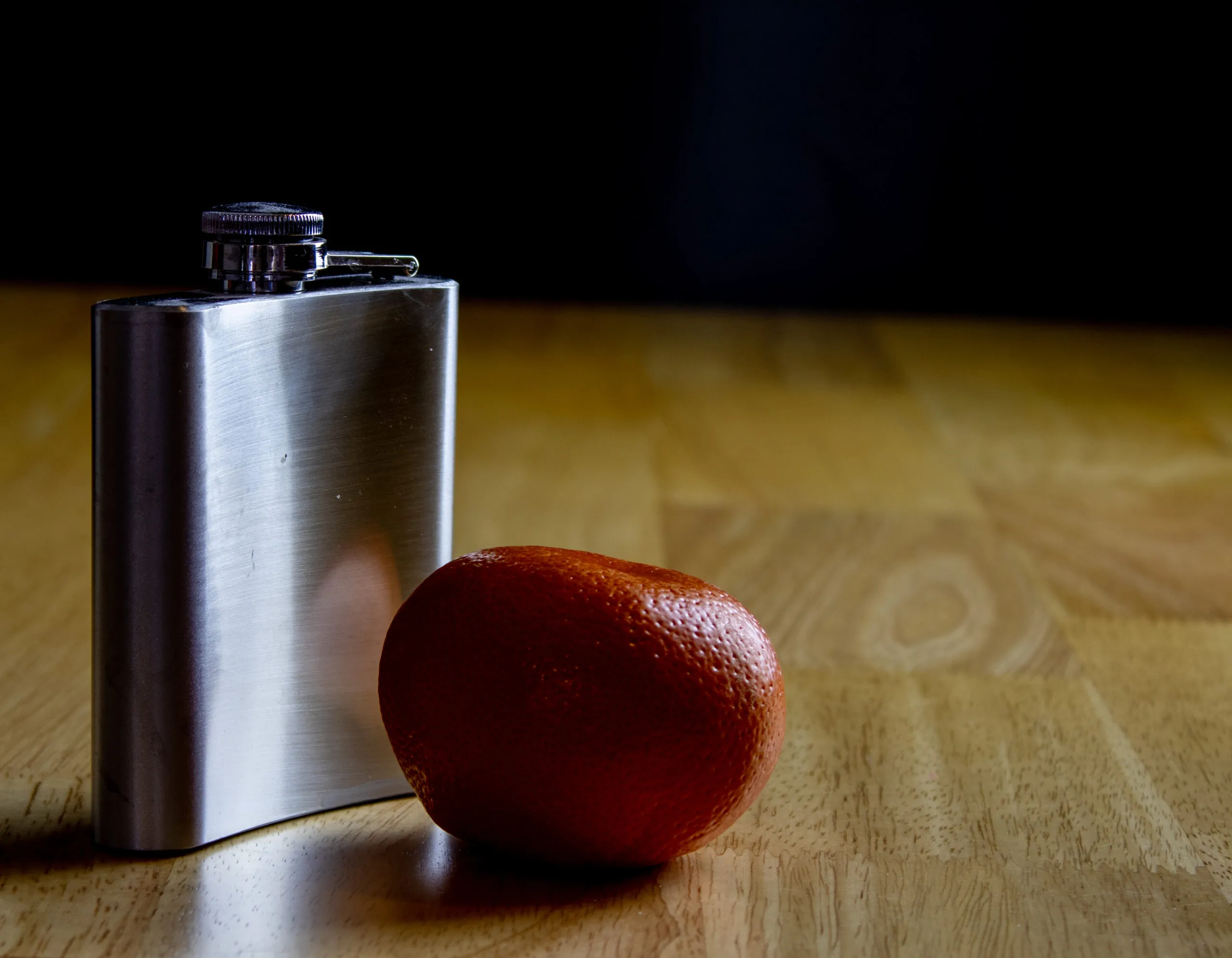 A metal flask and an orange arranged in directional light