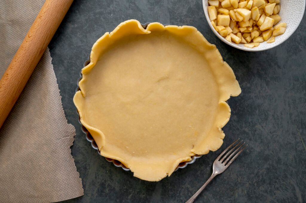 A pastry case being prepared in a pie dish on a dark kitchen surface