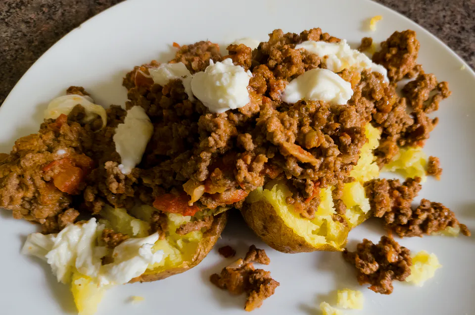 Baked potatoes filled with beef ragù and topped with a creamy garnish.