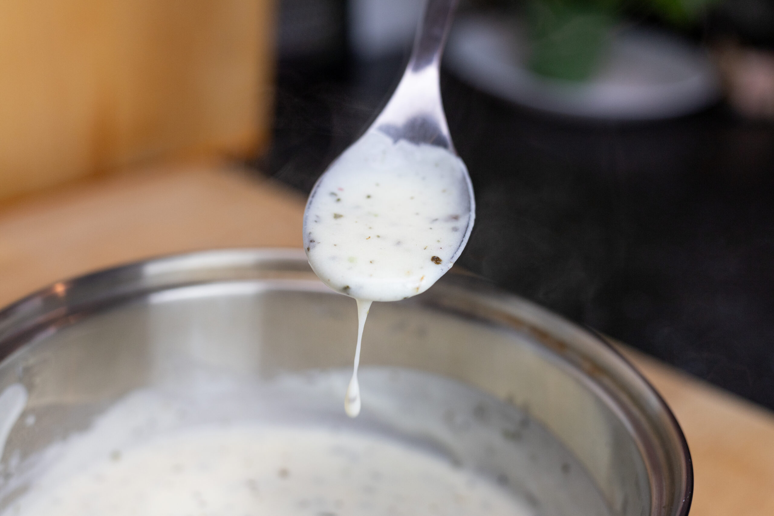Béchamel sauce dripping from a spoon into a saucepan.