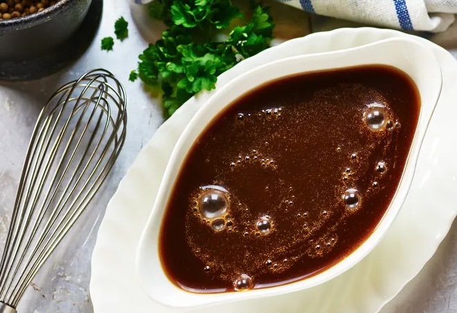Espagnole sauce in a white gravy boat beside a whisk.