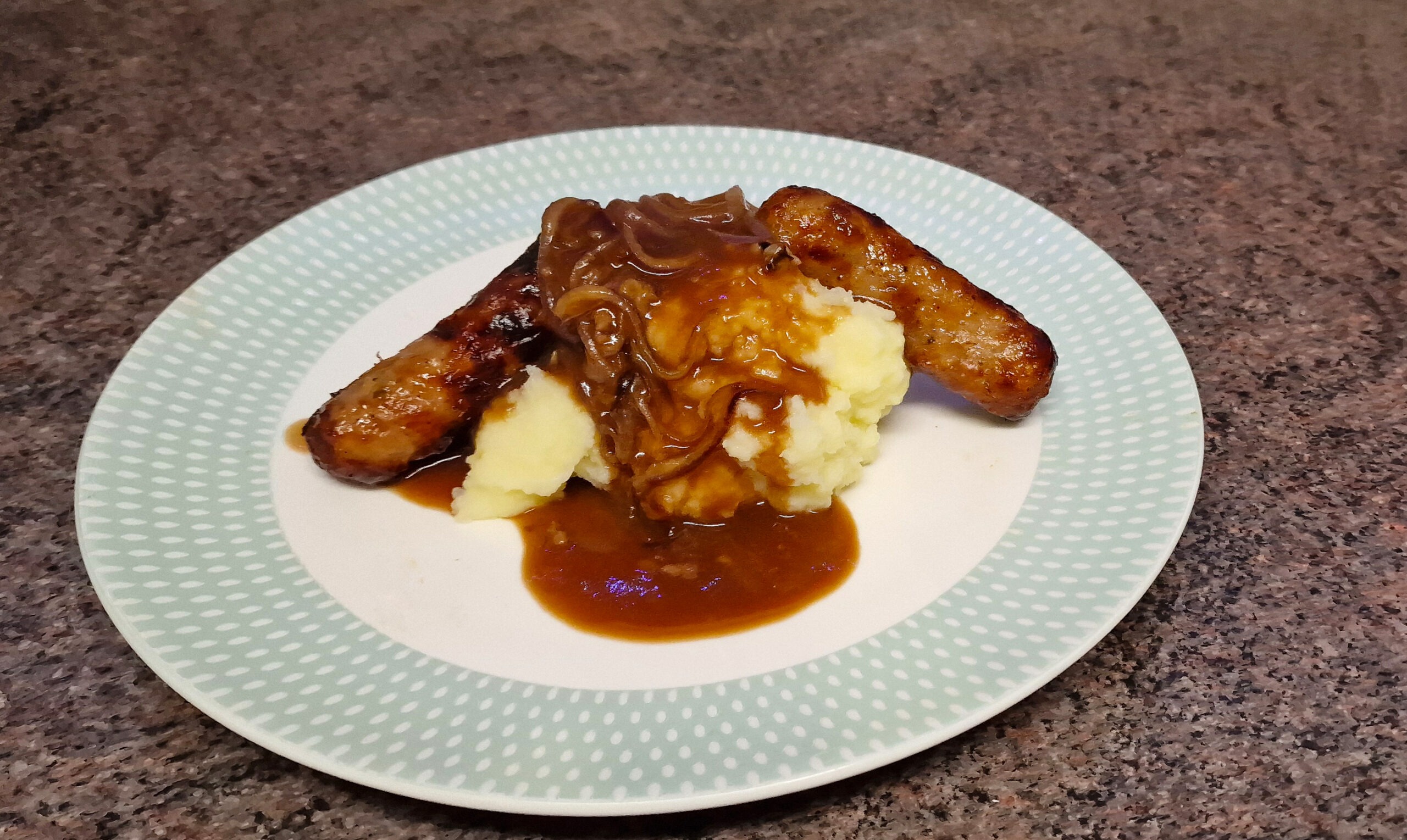 Bangers and mash with onion gravy on a dinner plate.